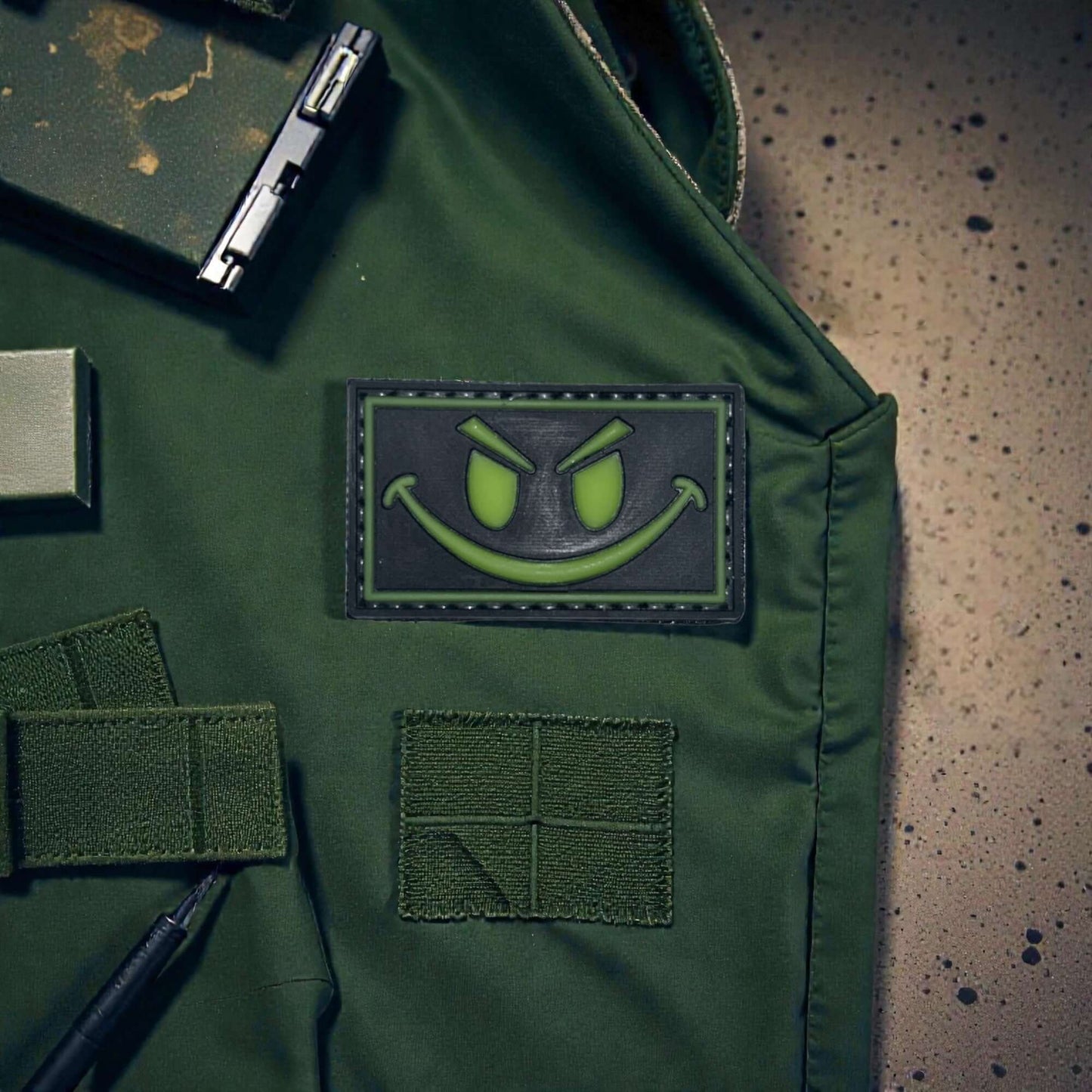 Smiley Glow Green PVC Patch on green vest with hook-and-loop backing, perfect accessory for gear.