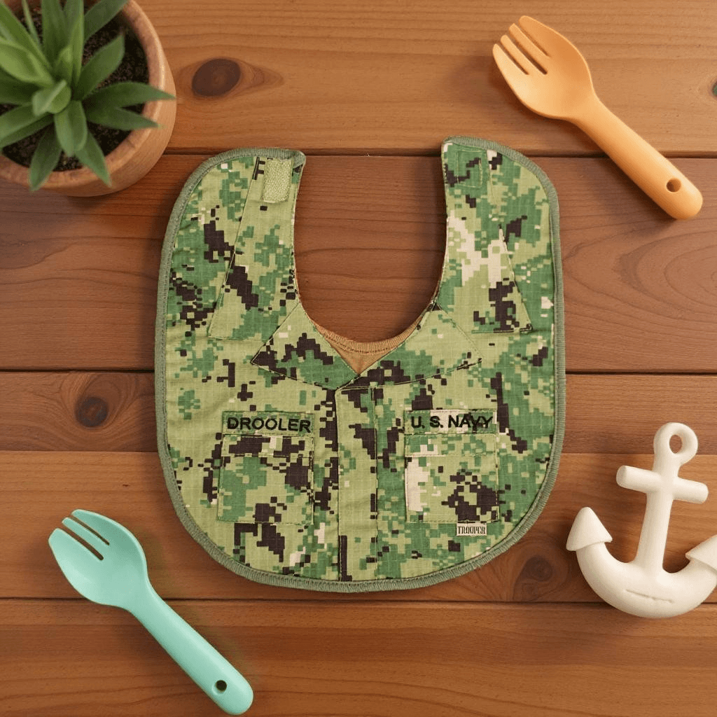 Navy NWU III Drooler Bib featuring simulated uniform design and embroidered name tags on wooden surface.