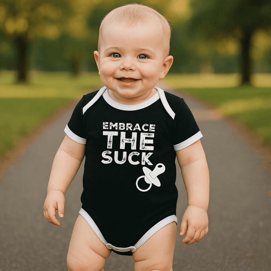Baby smiling in an 'Embrace the Suck' black bodysuit with a pacifier graphic.